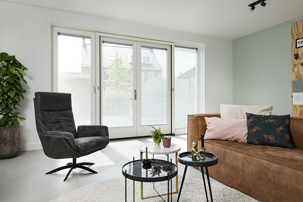 Woonkamer met zwarte stoel en bruine bank voor raam met inblindz